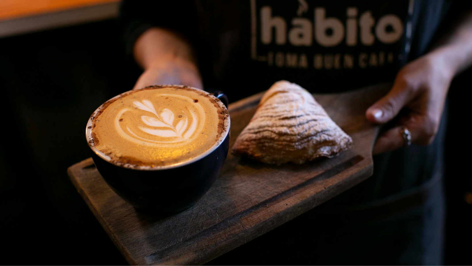 Un café de especialidad y una sfogiatella sobre un plato de madera.